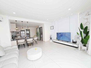 Een moderne woonkamer met een eethoek, een flatscreen televisie en een witte bank.