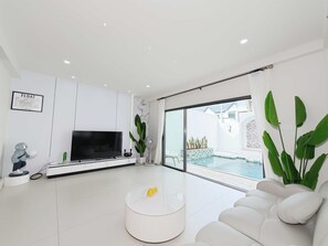 Een moderne woonkamer met een flatscreen-televisie, een ronde salontafel, een bank, een ventilator en uitzicht op een zwembad.
