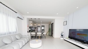 A modern living room with a sofa, a coffee table, a dining area with chairs, a kitchen in the background, and a TV on the wall. - POOL Villa KTV BBQ Friends Thepprasit (Muang Pattaya)