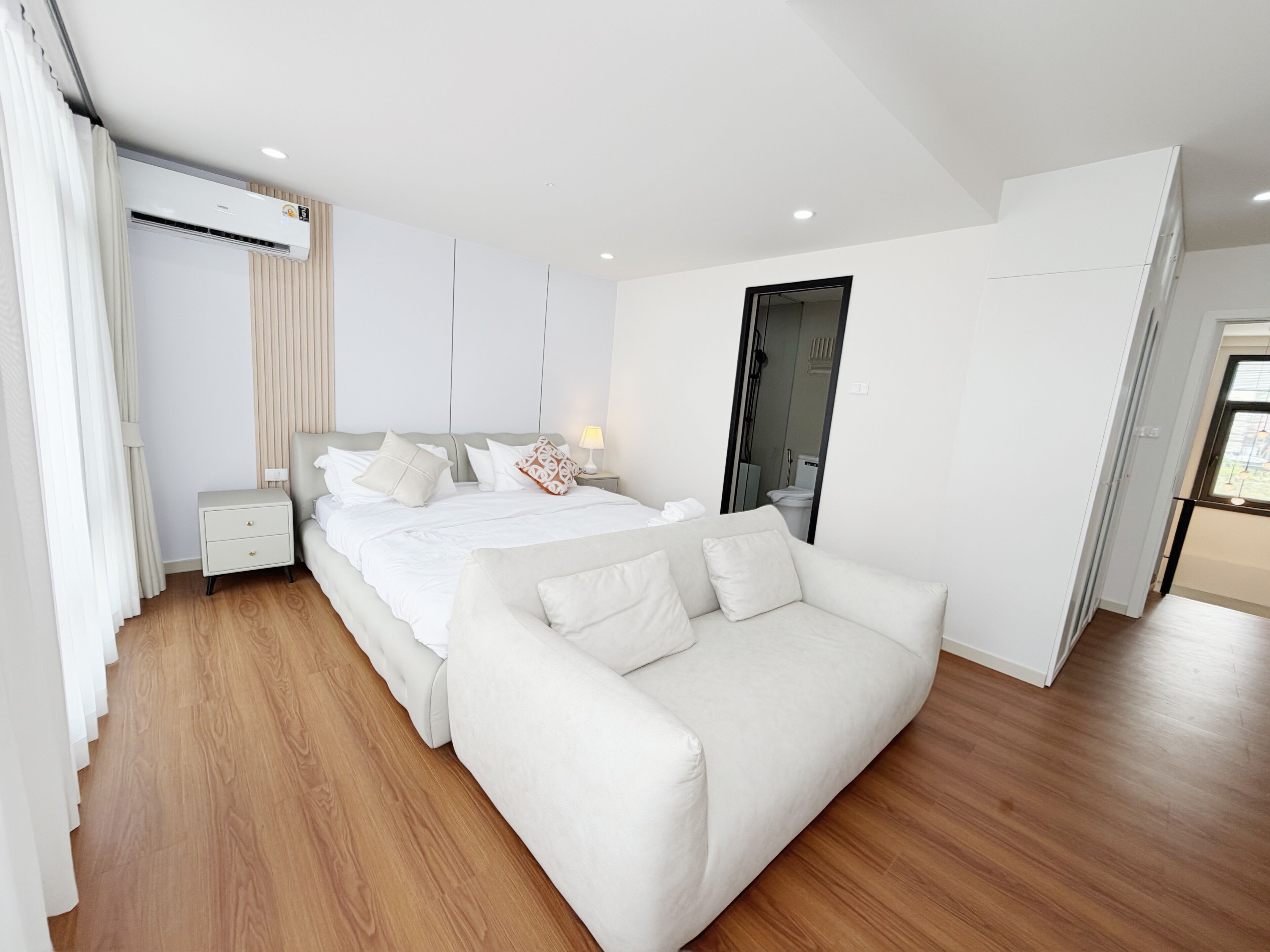 Een moderne slaapkamer met een bed, nachtkastjes, een bank, houten vloeren en een raam.