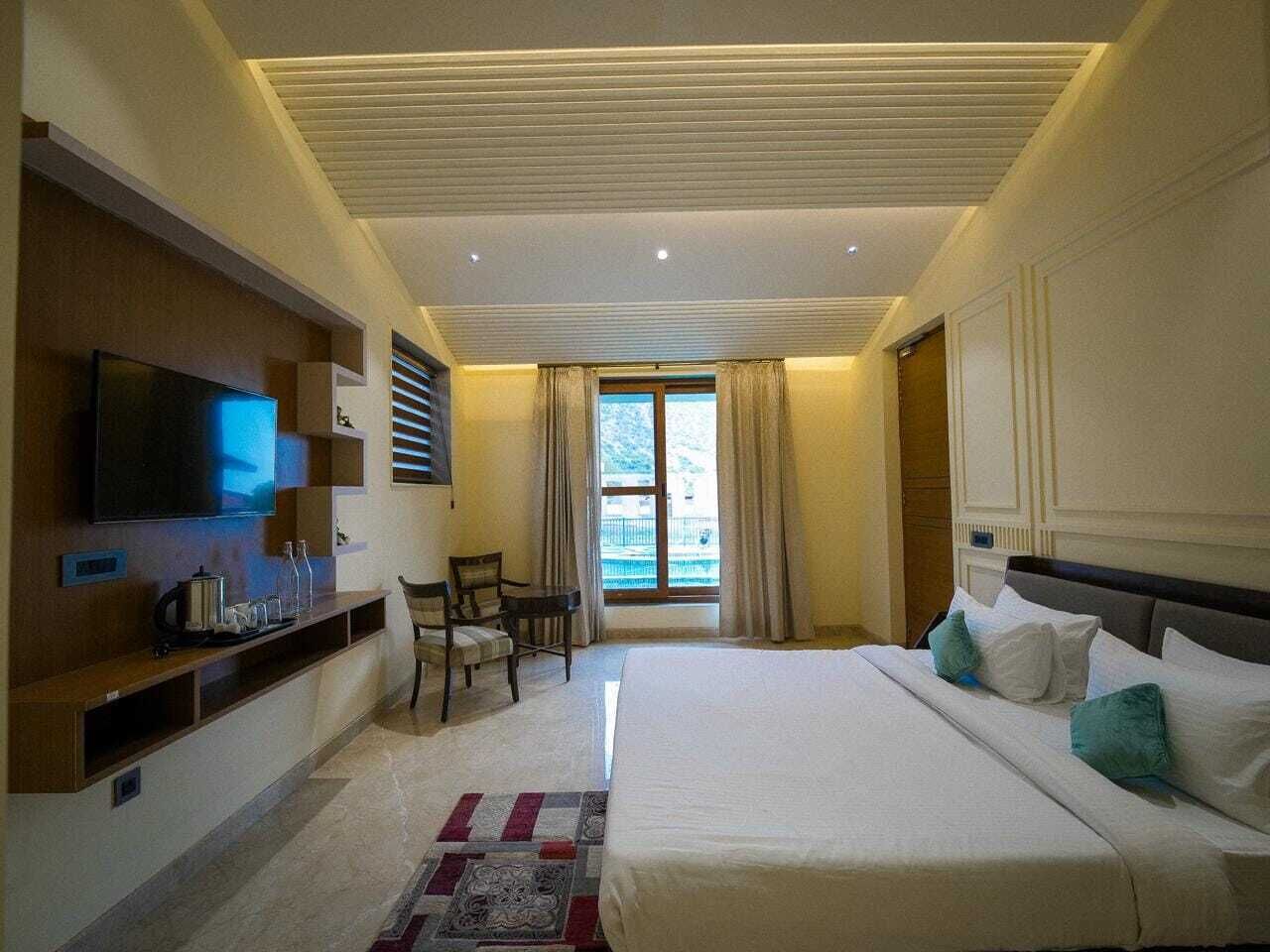 A hotel room with a large bed, a flat-screen TV, a seating area, and a window with curtains.