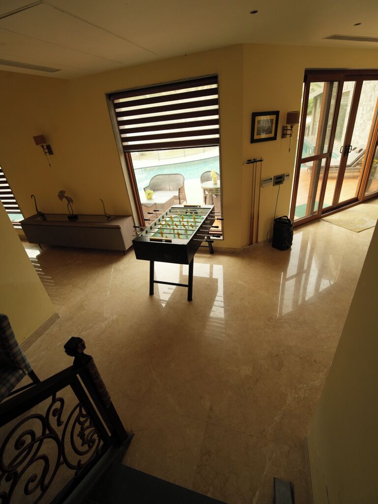 A room with a foosball table, a window with blinds, and a view of a pool.