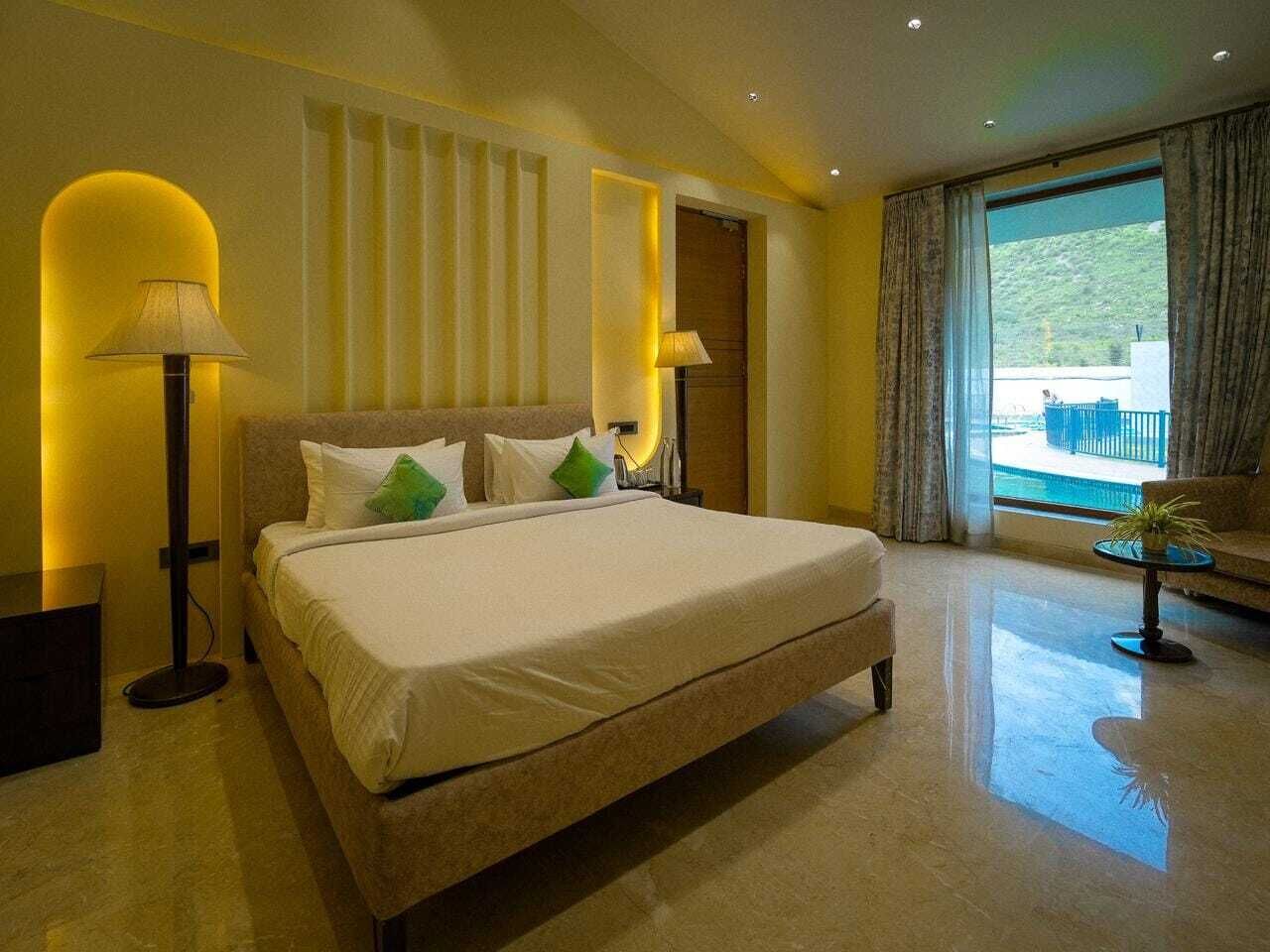 A hotel room with a large bed, two bedside lamps, a view of the outdoors, and a balcony.