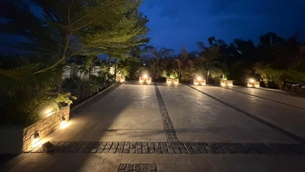 A paved courtyard with evenly spaced lights, surrounded by trees and plants. - Rosewood Manor BNB (Alwar)