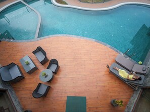 A pool area with lounge chairs and a sunbed, surrounded by a wooden deck. - Rosewood Manor BNB (Alwar)