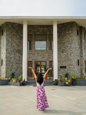 A woman in a long dress standing in front of a building with a stone facade and large windows. - Rosewood Manor BNB (Alwar)