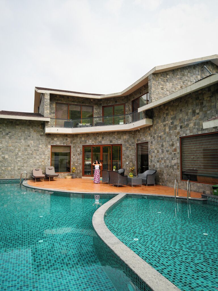 A modern building with a swimming pool, outdoor seating, and a person standing by the pool.