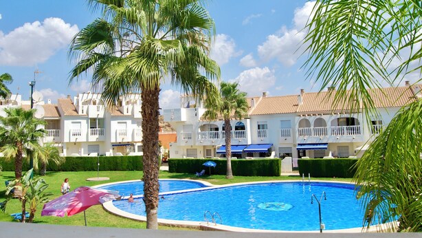 A swimming pool surrounded by palm trees and a building with balconies. - Duplex in Bolnuevo Ideal for Families with Pets (Bolnuevo)
