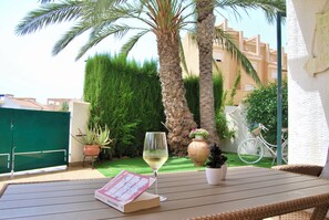 Eine Terrasse mit Tisch, einem Glas Weißwein, einem Buch und einem Fahrrad im Hintergrund.
