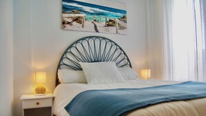 A neatly made bed with a blue blanket, a white pillow, and a headboard with a circular design. There is a nightstand with a lamp and a picture of a beach scene on the wall. - Duplex in Bolnuevo Ideal for Families with Pets (Bolnuevo)