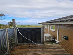 A wooden deck leading to a house with a black gate, a small attached structure, and a view of the sea. - 4 Star Holiday Home in Ebeltoft (Ebeltoft)