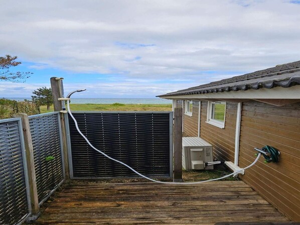 Un pontile in legno conduce a una casa con un cancello nero, una piccola costruzione adiacente e vista sul mare.