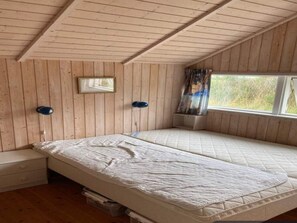 A room with wooden walls, a bed with a quilted mattress, a bedside table, a window with curtains, and a framed picture on the wall. - 4 Star Holiday Home in Ebeltoft (Ebeltoft)