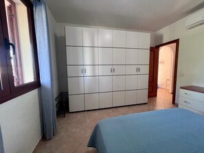 Ein Schlafzimmer mit großem Kleiderschrank, einem Bett und einem Fenster mit Vorhängen.