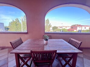 Una mesa de madera con cuatro sillas, una planta en maceta y vistas a través de dos ventanas arqueadas.