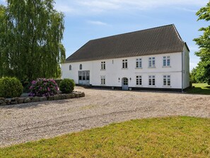 A two-story white building with a tiled roof, a gravel driveway, and a small garden with bushes and flowers. - 5 Star Holiday Home in Tonder (Tonder)