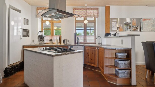 A kitchen with a central island, wooden cabinets, a stainless steel range hood, and a window with a view. - 5 Star Holiday Home in Tonder (Tonder)