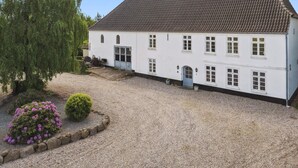 A two-story white building with a tiled roof, a gravel driveway, and a small garden with flowers and shrubs. - 5 Star Holiday Home in Tonder (Tonder)