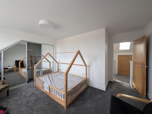 Une chambre à coucher avec un lit à baldaquin en bois, une lucarne, une armoire et une porte donnant sur une autre pièce.