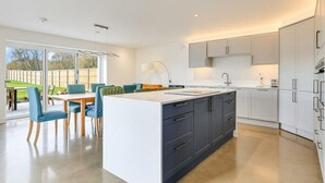 A modern kitchen with a central island, white cabinetry, and a dining area with blue chairs.