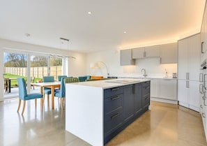 Une cuisine moderne dotée d’un îlot central, de meubles blancs et d’un coin repas avec des chaises bleues.