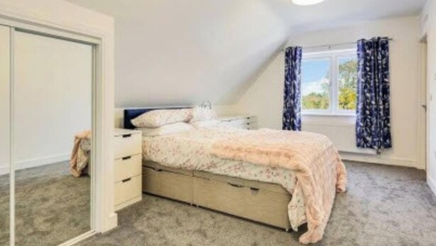 A bedroom with a bed, a dresser, a window with curtains, and a door.