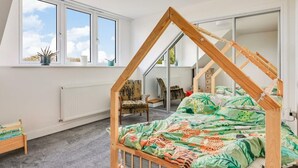 A bedroom with a sloped ceiling, a bed with a wooden frame, a window with a view, and a radiator.