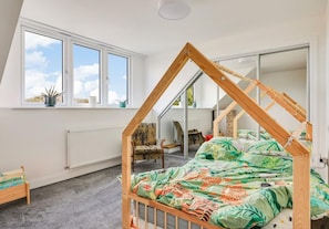 Une chambre avec un plafond en pente, un lit avec un cadre en bois, une fenêtre donnant sur un beau paysage et un radiateur.