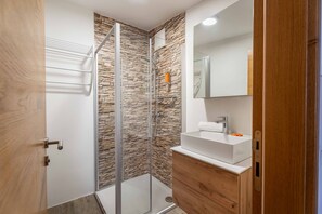 Un baño moderno con cabina de ducha de vidrio, un lavabo blanco y muebles de madera.
