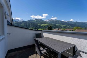 Un balcón con mesa y sillas de madera, vista a las montañas y cielo despejado.