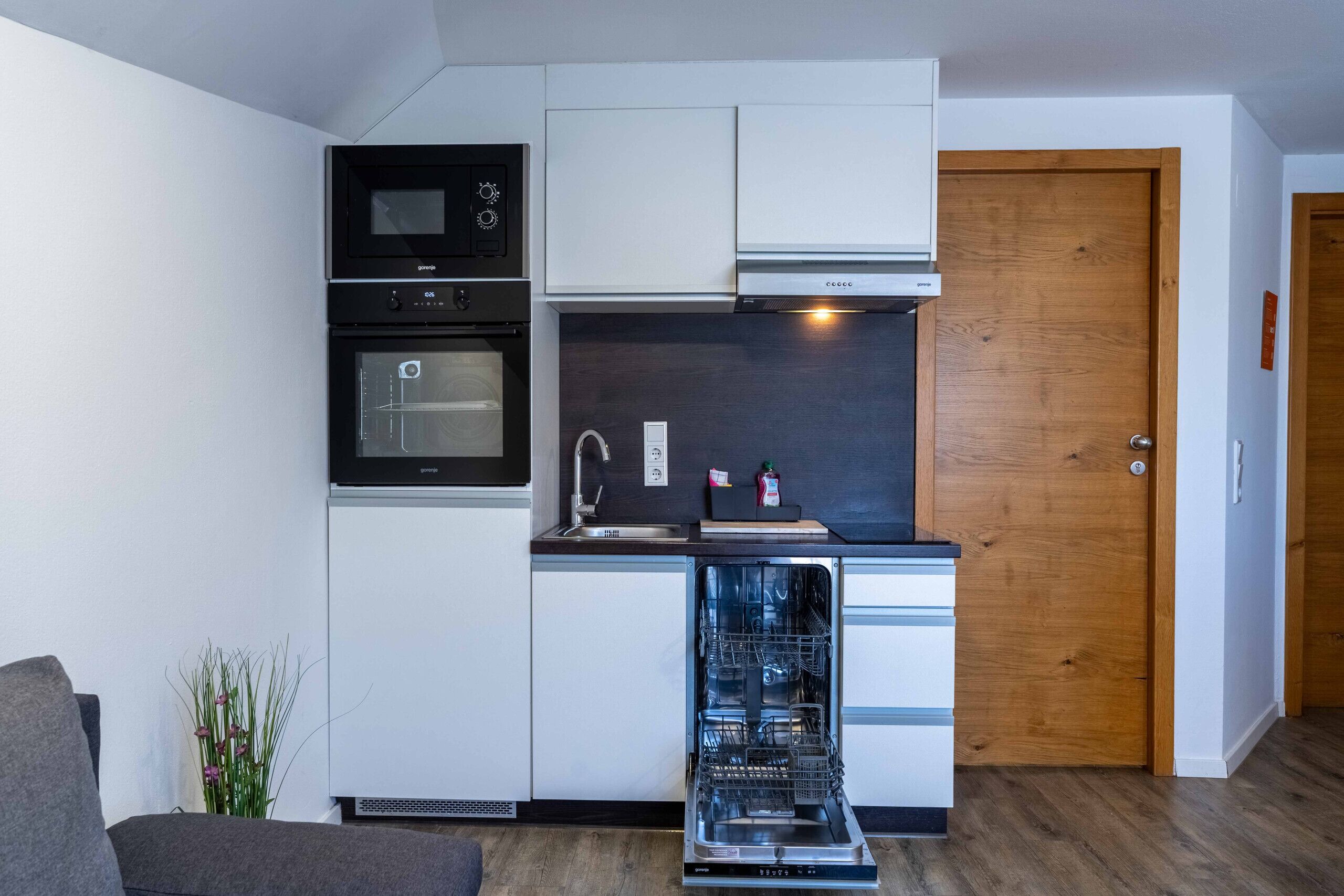 Een praktische keuken met een vaatwasser, oven, magnetron en een houten deur.