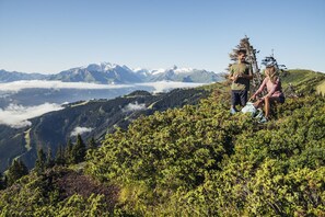 A mountainous landscape with a clear sky, a person standing with a backpack, and another person sitting on the ground. - Maiskogelblick Apartments - TOP 17 (Piesendorf)