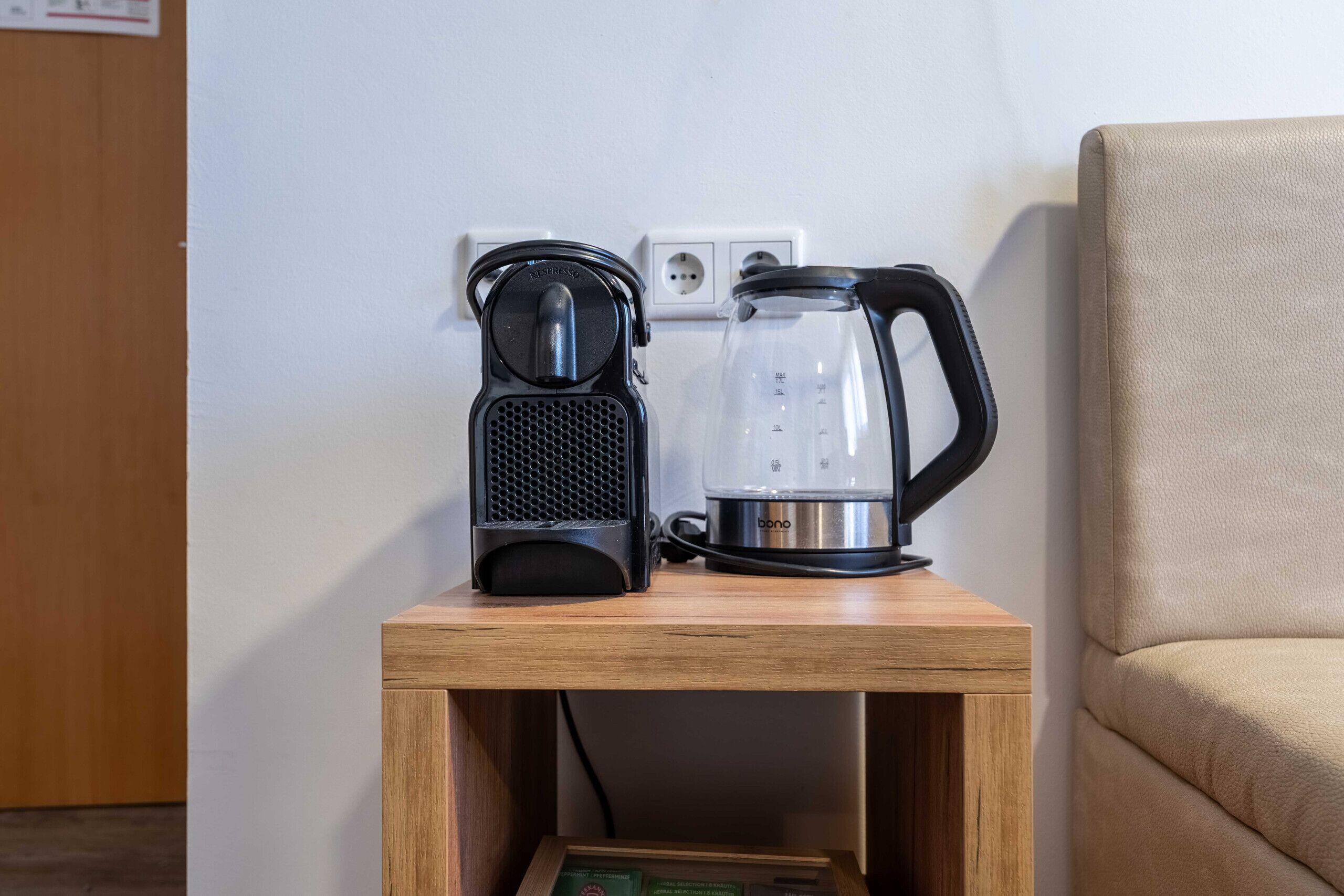 Une table de chevet en bois, sur laquelle se trouvent une machine à café et une carafe en verre.