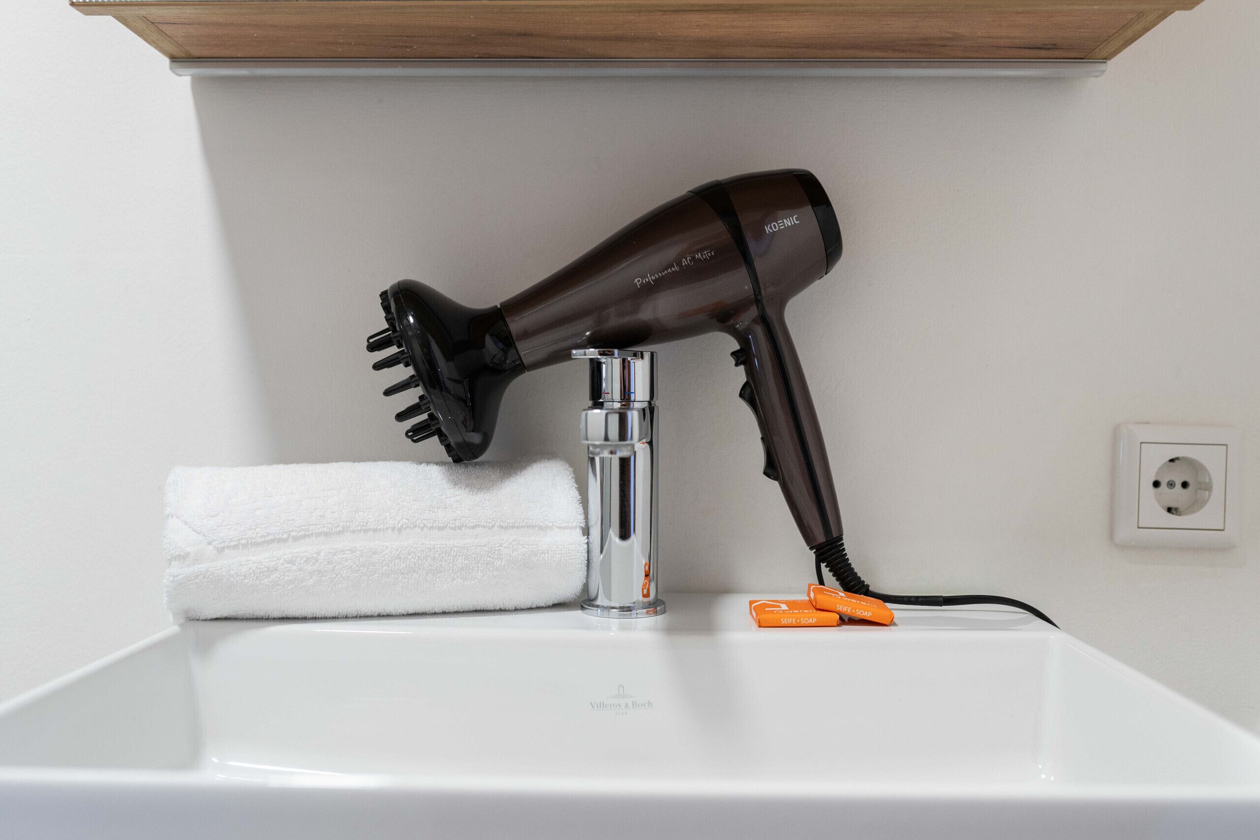 A hair dryer on a white sink with a towel and a power strip.