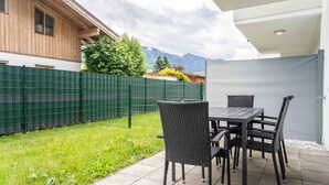 A patio with a table and chairs, a green fence, and a view of mountains. - Maiskogelblick Apartments - TOP 5 (Piesendorf)