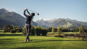 A person playing golf on a well-maintained course with a mountainous backdrop.
