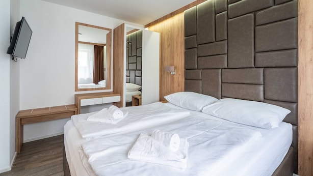 A hotel room with two beds, a wooden headboard, a flat-screen TV, and a mirror. - Maiskogelblick Apartments - TOP 5 (Piesendorf)