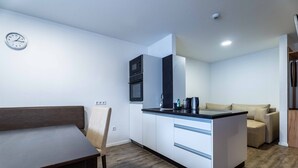 Et kompakt køkken med spiseplads, indbyggede hårde hvidevarer og en sofa.