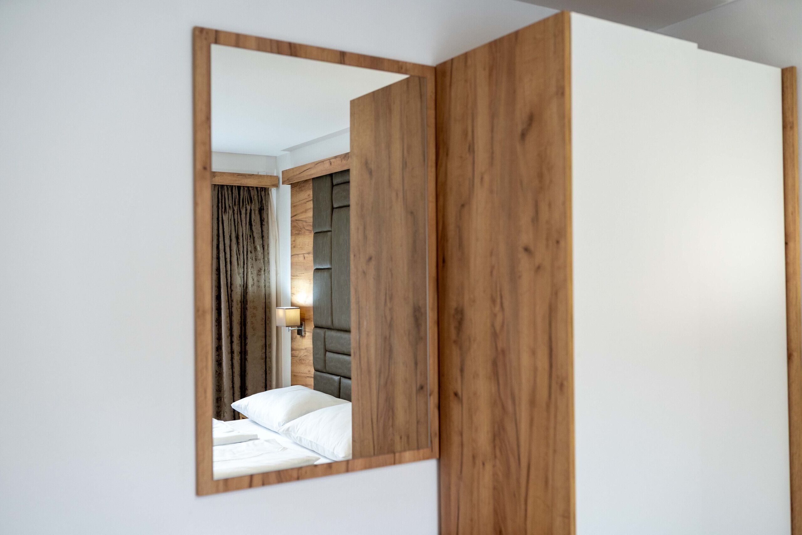 A room with a wooden headboard, a bed with white linens, and a wall-mounted light fixture.