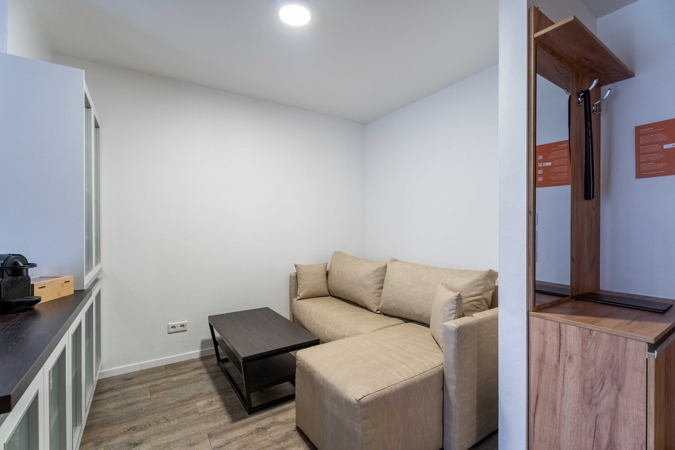 A small, modern room with a beige sofa, a small table, a wooden cabinet, and a shower area.