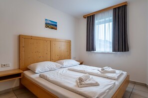 Una cama individual con cabecera de madera, ropa de cama blanca, una mesita de noche pequeña y una ventana con cortinas.