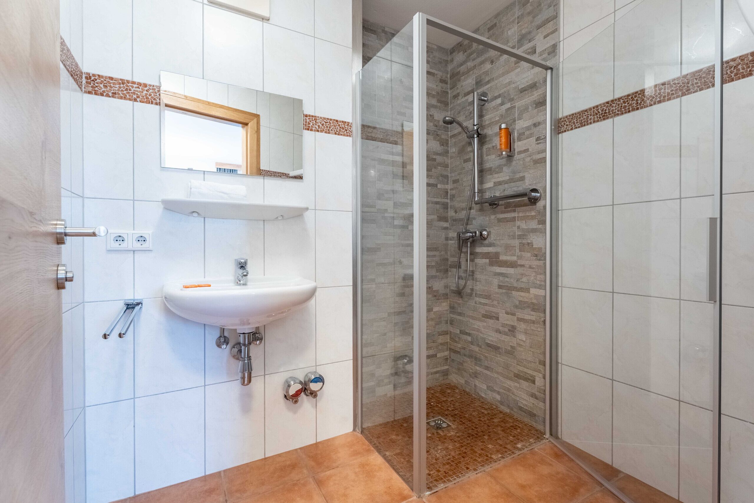 A bathroom with a glass shower enclosure, a white sink, and a mirror above it.