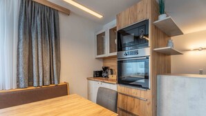 A modern kitchen with wooden cabinets, a built-in oven, and a dining area with a wooden table and bench. - Maiskogelblick Apartments - TOP 12 (Piesendorf)