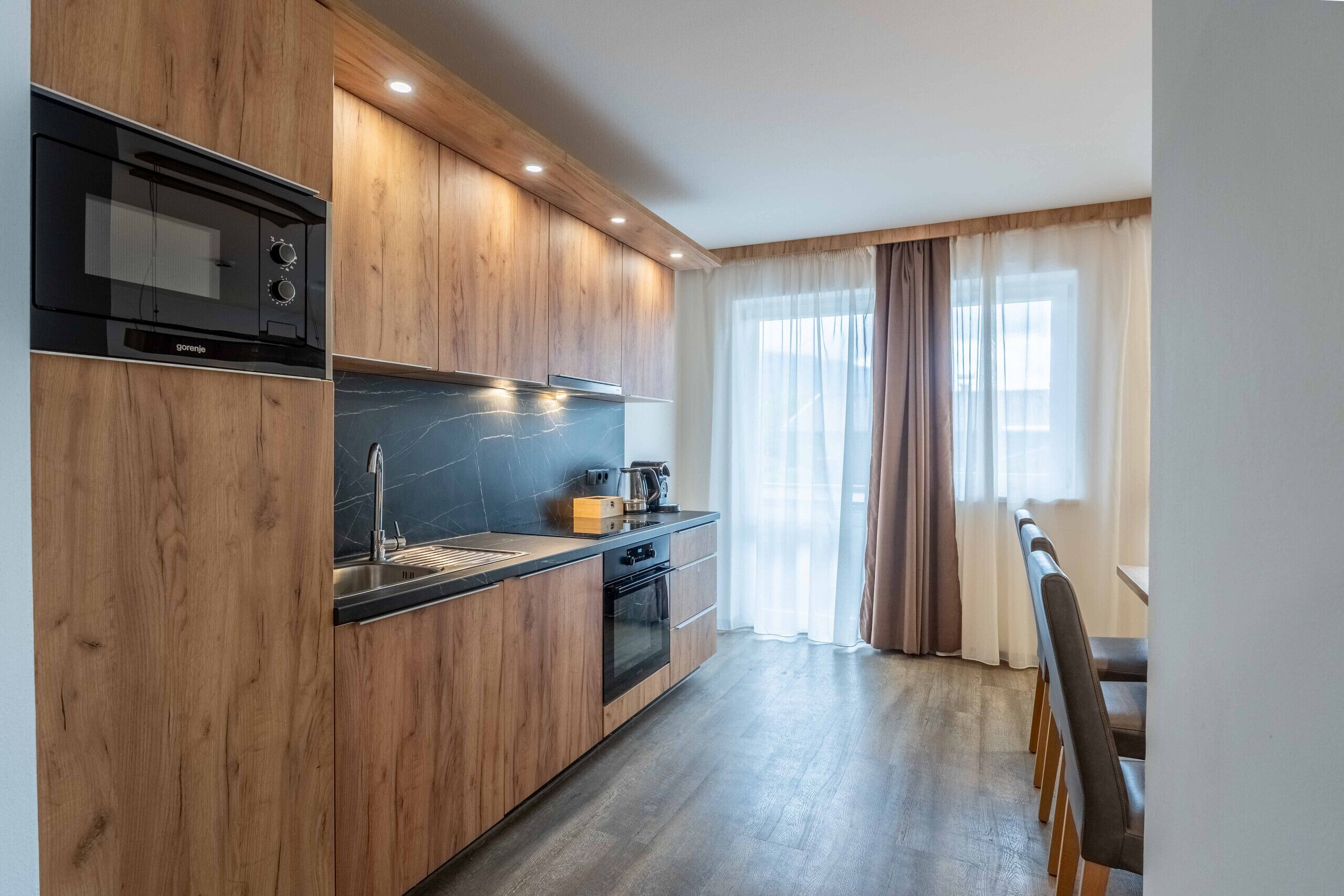 A modern kitchen with wooden cabinetry, a black stove, and a dining area with a table and chairs.