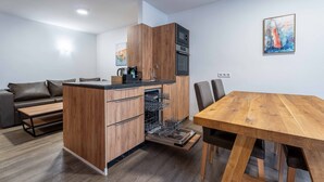 A compact kitchen with built-in appliances, a dining area with a wooden table, and a sofa in a living space. - Maiskogelblick Apartments - TOP 4 (Piesendorf)
