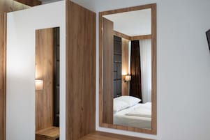Quarto moderno com um espelho grande, painéis de madeira, uma cama com roupa de cama branca e uma mesa de cabeceira com abajur.