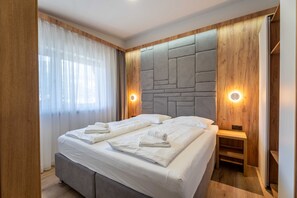 Una habitación de hotel moderna con una cama grande, paneles de madera e iluminación empotrada.