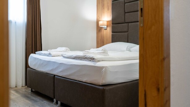 A hotel room with a bed, a wall-mounted light, and a wooden headboard. - Maiskogelblick Apartments - TOP 8 (Piesendorf)