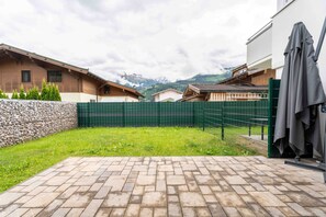 A courtyard with a brick patio, a green fence, and a stone wall. - Maiskogelblick Apartments - TOP 2 (Piesendorf)