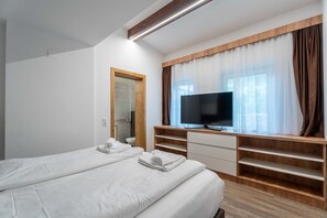 A hotel room with two beds, a TV, wooden shelving, and a window with curtains. - Maiskogelblick Apartments - TOP 2 (Piesendorf)
